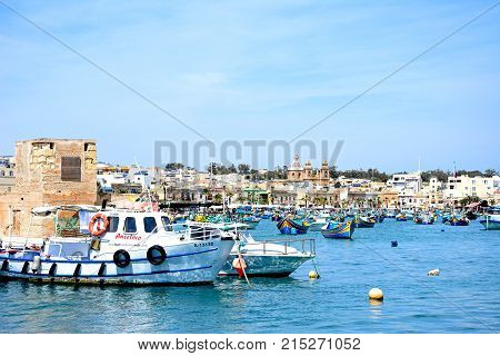 MARSAXLOKK, MALTA - APRIL 1, 2017 - Traditional Maltese Dghajsa fishing boats in the harbour with waterfront buildings to the rear Marsaxlokk Malta Europe, April 1, 2017.