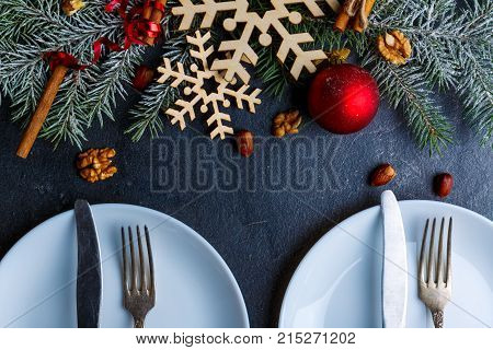 The served table with two plates and cutlery is decorated with Christmas tree branches. View from above. Indoors.