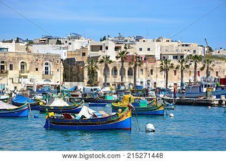 MARSAXLOKK, MALTA - APRIL 1, 2017 - Traditional Maltese Dghajsa fishing boats in the harbour with waterfront buildings to the rear Marsaxlokk Malta Europe, April 1, 2017.