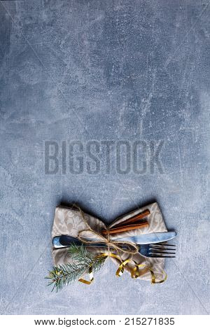 On a background with a place for an inscription a serving fork and a knife in a napkin and a fur-tree branch. View from above. Indoors.