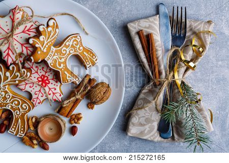 Close-up. A plate with delicious Christmas cookies of different shapes with colored sugar icing, next to the plate there are cutlery wrapped in a tissue napkin and decorated with a Christmas tree branch, cinnamon sticks and a golden ribbon. Christmas atmo