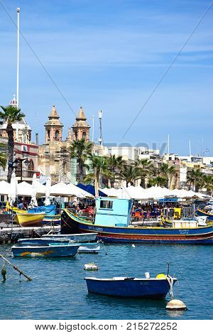 MARSAXLOKK, MALTA - APRIL 1, 2017 - Traditional Maltese Dghajsa fishing boats in the harbour with the parish church of Our Lady of Pompei to the rear Marsaxlokk Malta Europe, April 1, 2017.