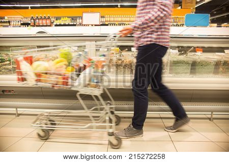 Low section view of unrecognizable man pushing shopping cart in blurred motion while choosing groceries in supermarket