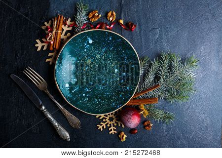 On a dark surface, a creative plate in a dark glossy surface, tableware, a Christmas tree branch is decorated with red balls and wooden snowflakes and a few cinnamon sticks. Close-up. Indoors.