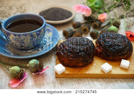 Sweet bun with flax seed and poppy and cup of tea on table.