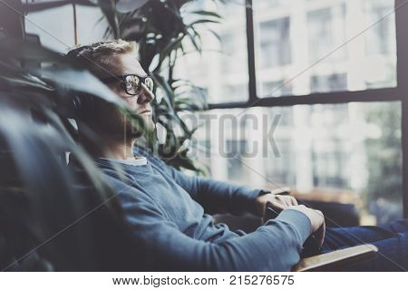 Attractive young man wearing glasses casual clothes.Man sitting in vintage armchair modern loft studio and relaxing whith headphone music. Blurred background.Horizontal