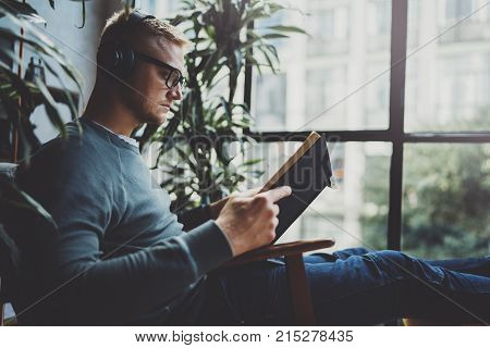 Portrait handsome young man wearing glasses casual clothes holding book hands.Man sitting in vintage armchair modern loft studio reading book. Blurred background.Horizontal