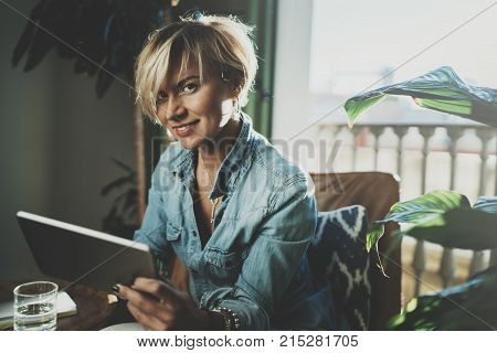 Smiling young woman wearing casual clothes and using electronic device while spending relax time in vacation travel.Attractive woman owner communicating on digital tablet.Blurred background