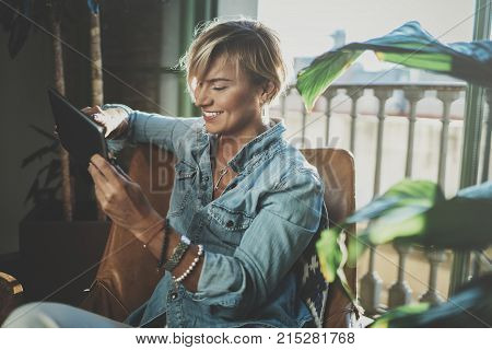 Smiling young woman wearing casual clothes and using electronic device while spending relax time in vacation travel.Attractive woman owner communicating on digital tablet.Blurred background