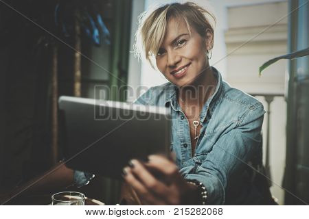 Smiling young woman wearing casual clothes and using electronic device while spending relax time in vacation travel.Attractive woman owner communicating on digital tablet.Blurred background