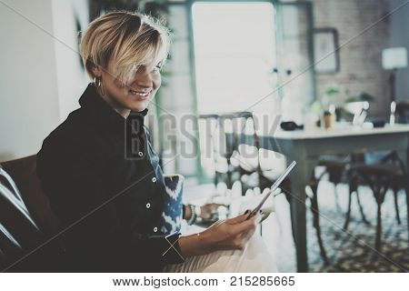 Smiling young woman wearing casual clothes and using electronic device while spending relax time in vacation travel.Attractive woman owner communicating on digital tablet.Blurred background