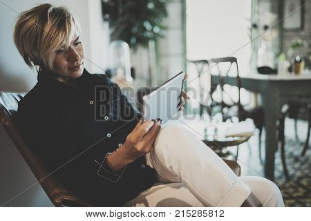 Smiling young woman wearing casual clothes and using electronic device while spending relax time in vacation travel.Attractive woman owner communicating on digital tablet.Blurred background