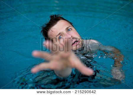Drowning caucasian man in swimming pool asking for help. He stretching his hands in fear. Emotional stress in dangerous situation. Do not know how to swim.