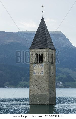 Church under water drowned village mountains landscape and peaks in background. Reschensee Lake Reschen Lago di Resia. Italy Europe Südtirol South Tyrol Upper Adige Alto Adige