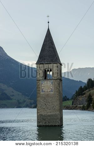 Church under water drowned village mountains landscape and peaks in background. Reschensee Lake Reschen Lago di Resia. Italy Europe Südtirol South Tyrol Upper Adige Alto Adige
