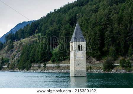 Church under water drowned village mountains landscape and peaks in background. Reschensee Lake Reschen Lago di Resia. Italy Europe Südtirol South Tyrol Upper Adige Alto Adige