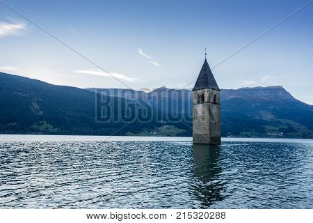 Church under water drowned village mountains landscape and peaks in background. Reschensee Lake Reschen Lago di Resia. Italy Europe Südtirol South Tyrol Upper Adige Alto Adige
