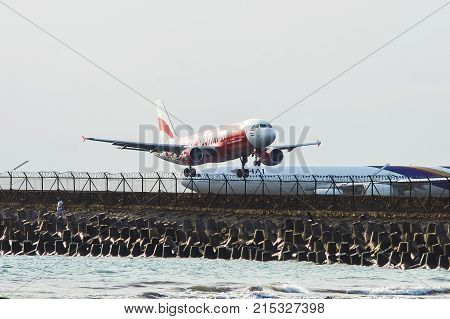 Bali Indonesia - November 25 2012: AirAsia Airbus A320 landing at Ngurah Rai International Airport on runway protruding in sea. Airbus A340 Thai Airways in the background