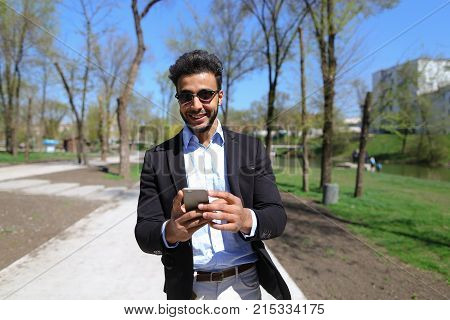 Man hold phone in hand and talking with mom. Son has dimple on cheeks, beard, short hair and long nose. Person dressed in black jacket and blue shirt. Concept of new apps modern technologies and long talks and cheep tariff plans.