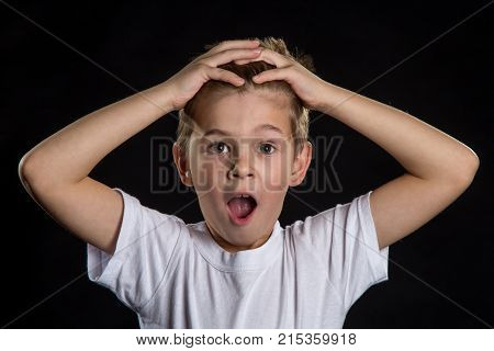 Shocked and surprised boy with open eyes and mouth on the black background. Sincere emotions of people.