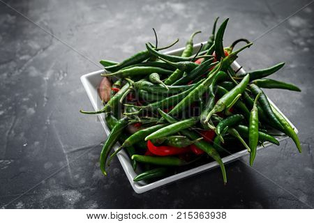 Green, red chilli Peppers in white bowl on black background.