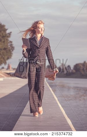 Vertical orange tonted shot of a beautiful blond woman walking with paper bags bag and tablet along the promenade