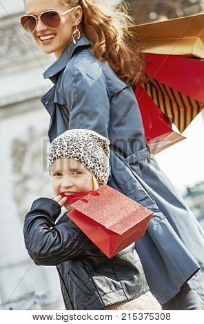 Stylish autumn in Paris. smiling young mother and child with shopping bags near Arc de Triomphe in Paris France walking