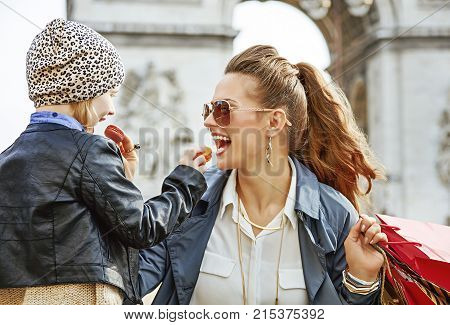 Stylish autumn in Paris. smiling young mother and daughter with shopping bags near Arc de Triomphe in Paris France eating macaroons