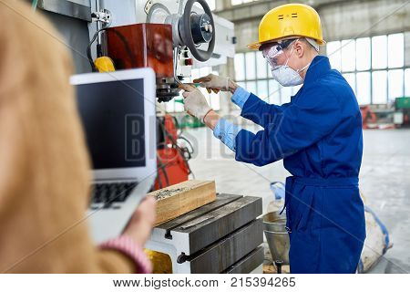 Concentrated factory worker in protective mask and goggles regulating machine in workshop