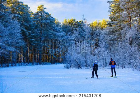 A girl and a guy with a red backpack go skiing on a frozen forest river