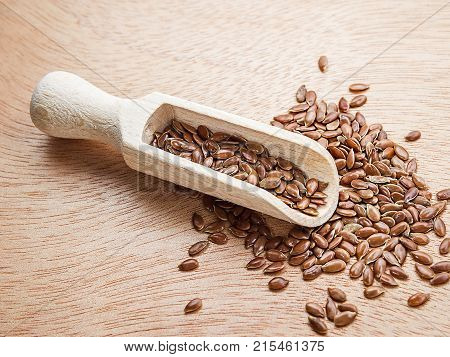 Flax seeds in a wood spoon on a wooden background. Flaxseed is scattered from a scoop.