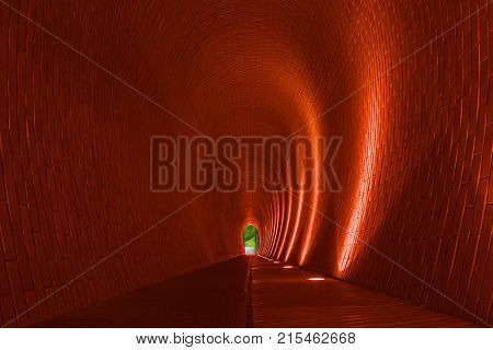 Empty long arched brick pedestrian tunnel Prague. Orange brick walls strip of lighting lamp. Bright arch. Underground mysterious footpath for walkers. Underpass and nature at end of tunnel concept