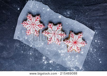 Close-up, top view, on parchment paper, sprinkled with powdered sugar, on the gray table lie New Year's biscuits in the form of snowflakes.