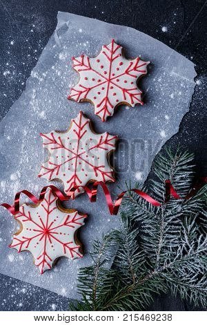 Close-up, top view, on parchment paper, sprinkled with powdered sugar, on the gray table lie New Year's biscuits in the shape of a snowflake, next to a red ribbon and spruce spruce.