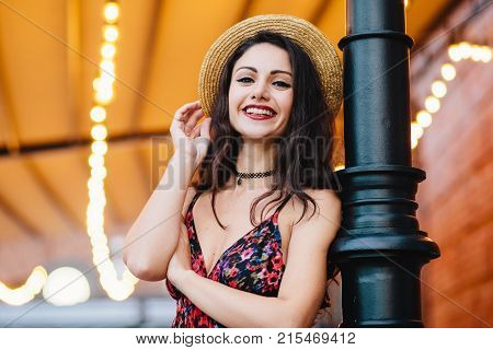 Excited Female With Dark Hair, Shinig Eyes And Red Lips, Dressed In Dress And Summer Hat, Posing At