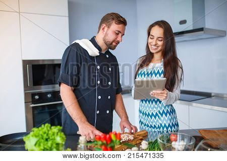 Young couple in the kitchen preparing food for dinner, watching the recipe on the tablet. Concept of cooking, family.
