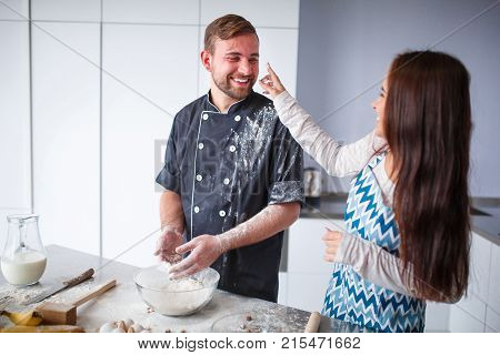 A young couple in the kitchen, cooking, fooling around, throwing flour, a girl wiping the flour on her husband's face. Concept of cooking, family.