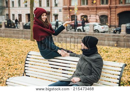 Good Looking Female Wers Knitted Hat And Scarf, Throws Yellow Leaves In Air, Holds Boyfriend`s Hand,