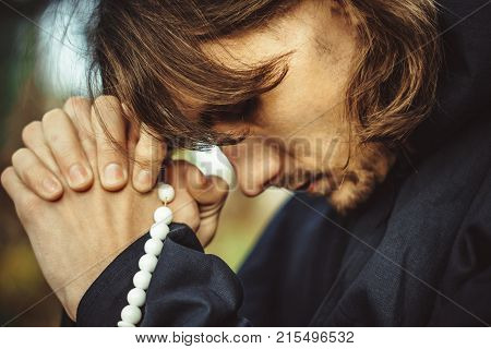 a monk in a black robe praying in the woods on his knees