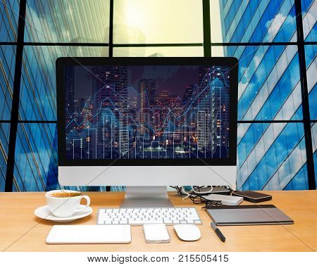 Workspace with computer desktop on the wood table with trading graph at the screen on the blurred photo of cityscape building background