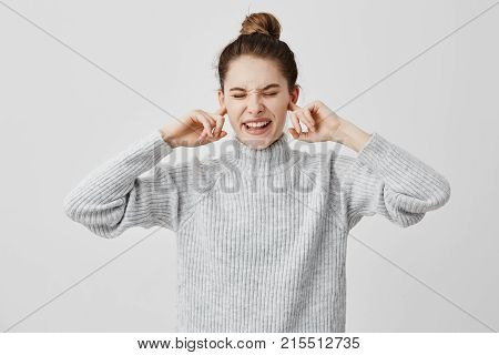 Annoyed woman plugging ears with fingers and screwing up her eyes in displeasure. Brunette female covering ears complaining on loud music from outside. Human feelings, reactions