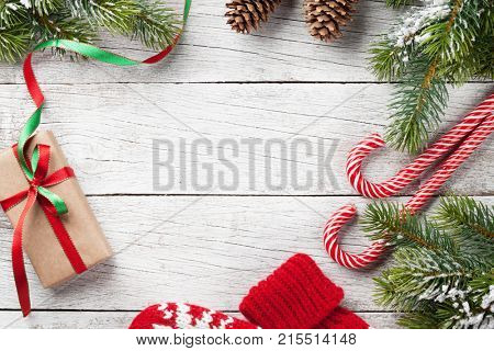 Christmas gift box, candy cane, mittens and snow fir tree on wooden table. Top view with space for your greetings