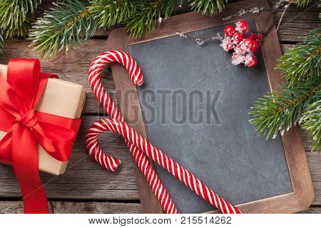 Christmas gift box, candy cane and snow fir tree on wooden table. Top view with chalkboard for your greetings