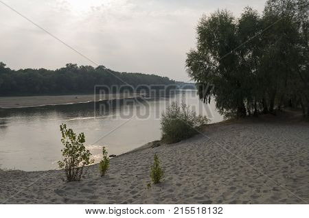 Wide river flowing across green forest. Fall. Evening. Reflections of trees in the calm water. Sundown