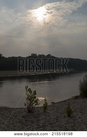 Wide river flowing across green forest. Fall. Evening. Reflections of trees in the calm water. Sundown