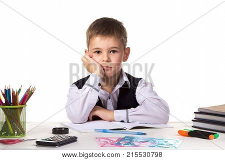 Cute bored pupil sitting at the desk with hand under the chin surrounded with stationery.