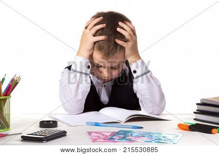 Bewildered pupil sitting with lowered eyes at the desk with hands over the head surrounded with stationery.