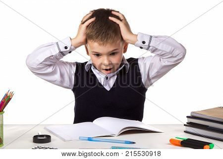 Stressed bewildered pupil sitting at the desk with hands over the head surrounded with stationery.