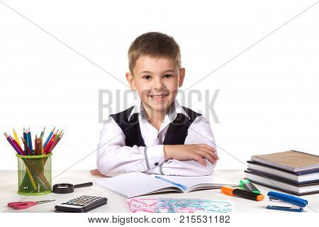 Smiling cheerful excellent pupil sitting still at the desk with white background.
