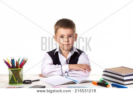 Smart serious excellent pupil sitting still at the desk with white background.